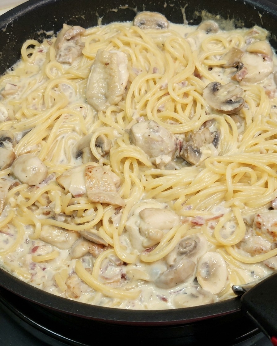 Spaghetti wymieszane z kremowym sosem na patelni.