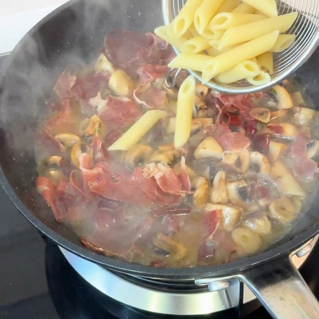 Ugotowany makaron penne przekładany do patelni z sosem.
