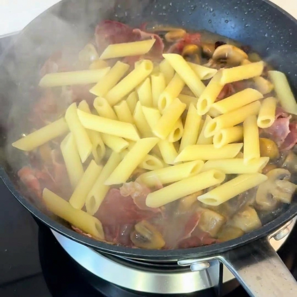 Makaron penne z pieczarkami i szynką doprawiany czarnym pieprzem.