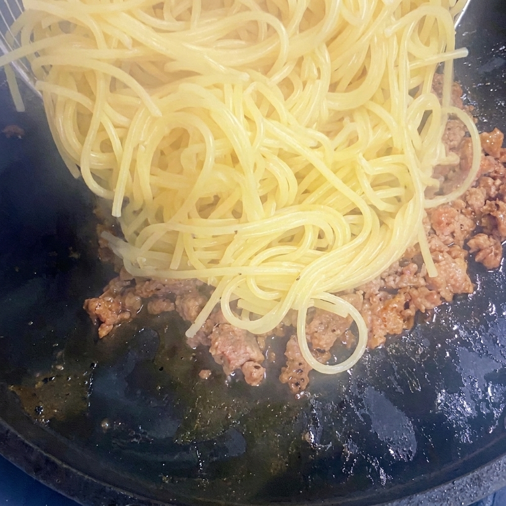 Ugotowany makaron spaghetti dodawany do patelni z mięsem.