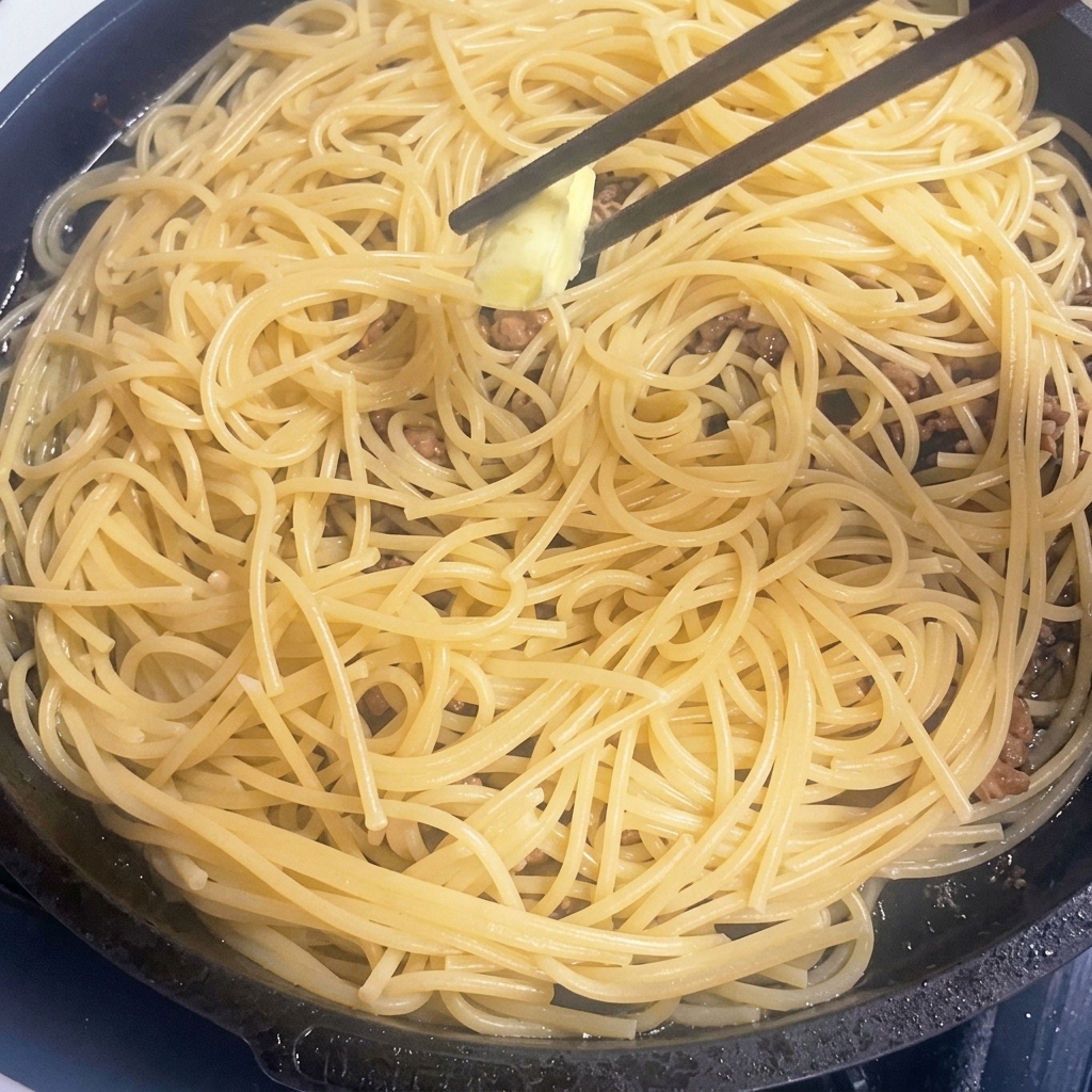 Kawałek masła rozpuszczający się na gorącym makaronie z mięsem.