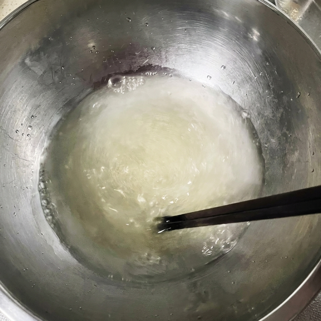 Pałeczki mieszające mętny roztwór wody, drożdży i soli w metalowej misce.