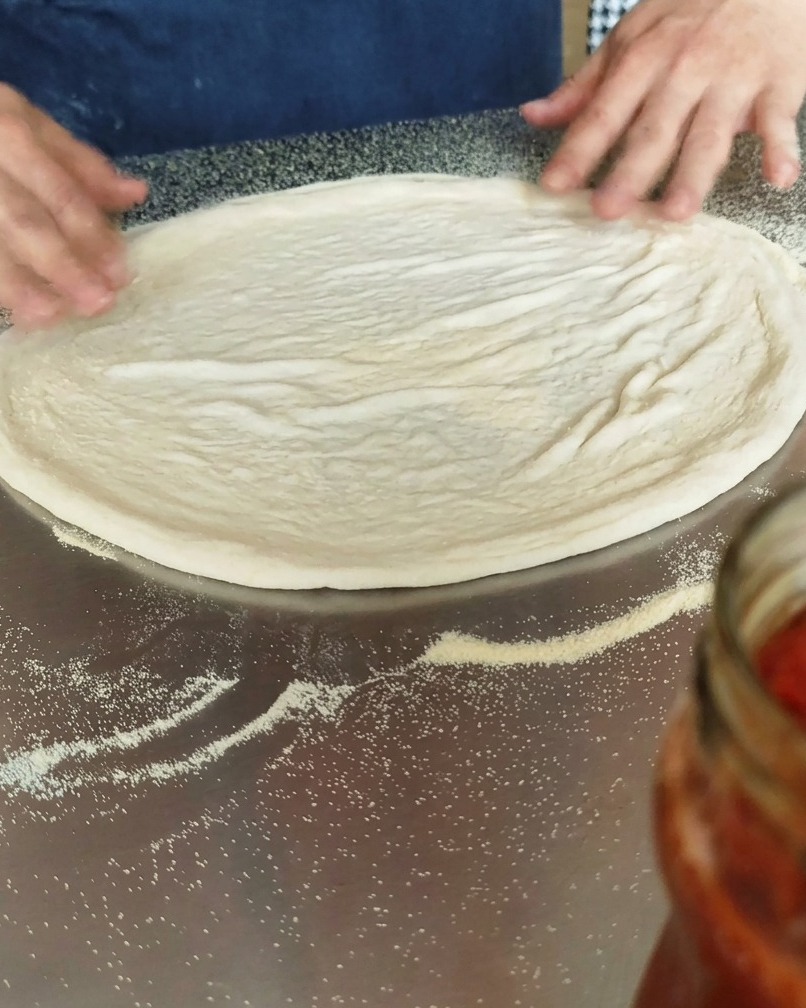 Okrągłe ciasto na pizzę leżące na blacie z semoliną.