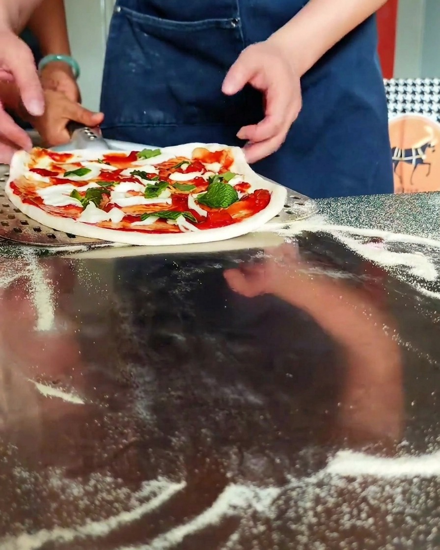Dłonie wsuwające łopatę pod pizzę.