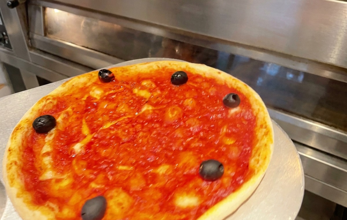 Forma z pizzą wsuwana do gorącego, profesjonalnego piekarnika w celu upieczenia.