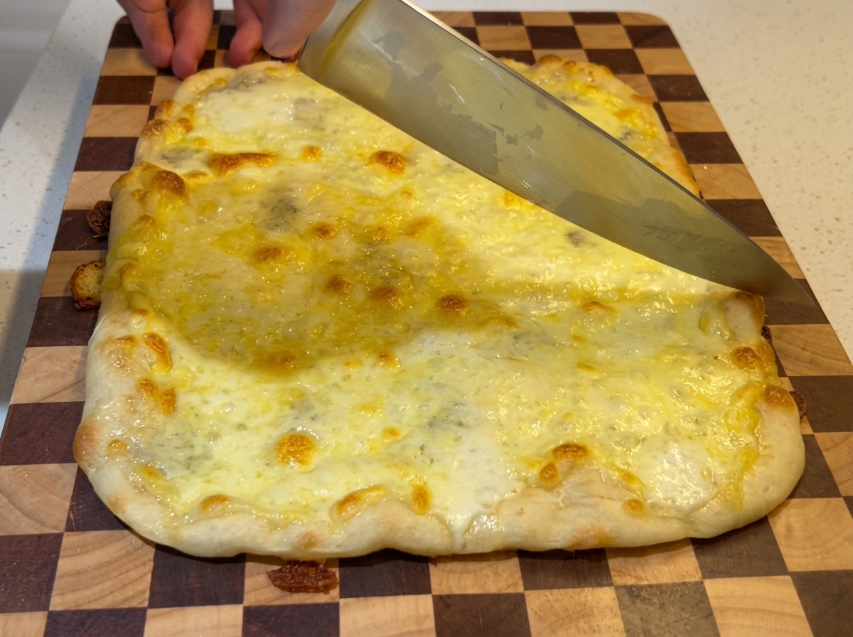 Duży nóż szefa kuchni krojący pizzę na prostokątne kawałki.
