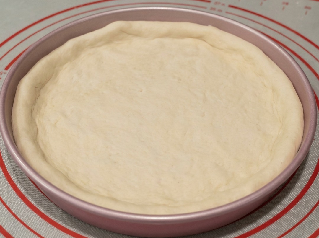 Ciasto dopasowane do metalowej blachy do pizzy o średnicy 23 cm z brzegami uformowanymi ręcznie.