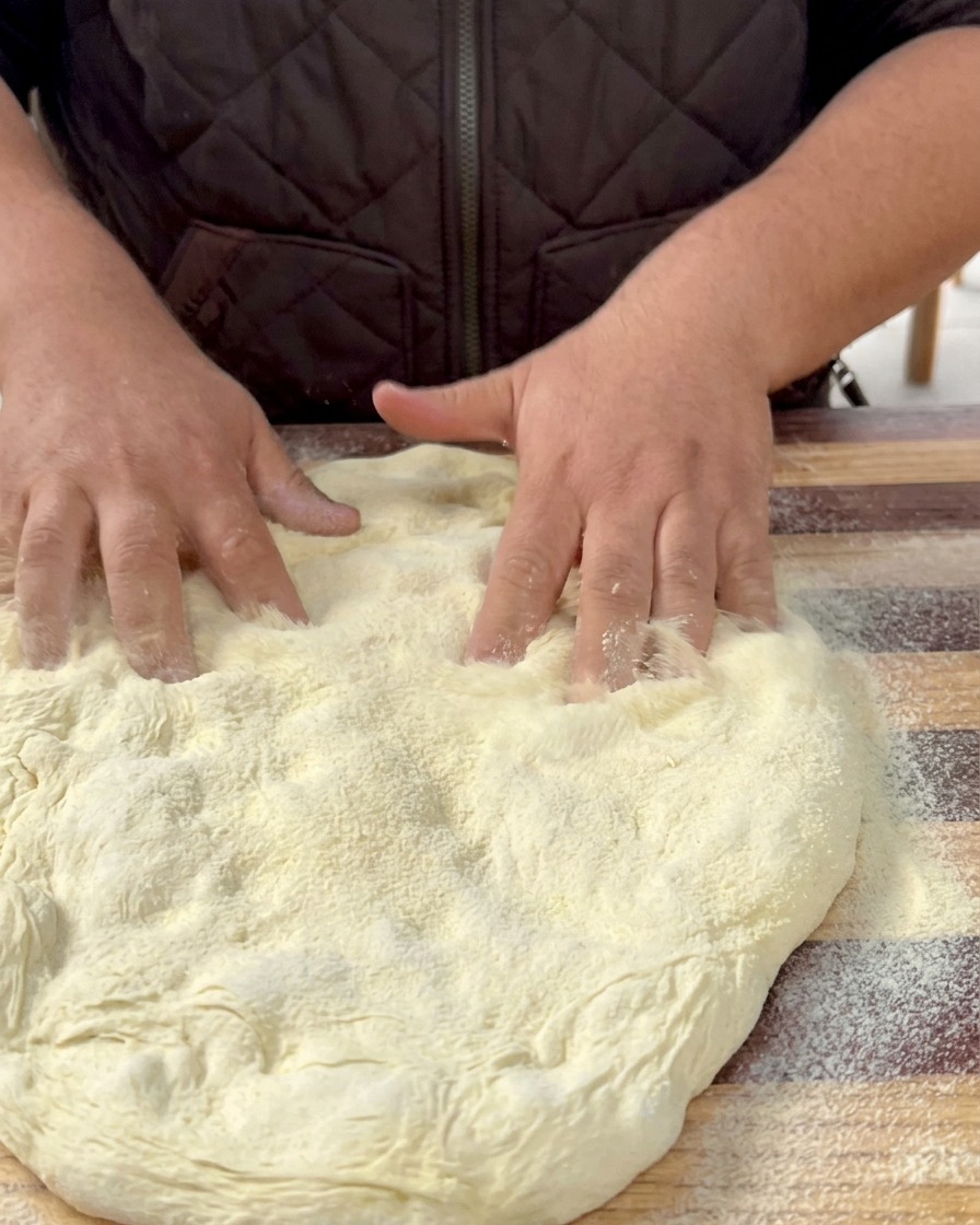 Rozciągnięte ciasto na pizzę leżące na blaszce wyłożonej papierem do pieczenia.