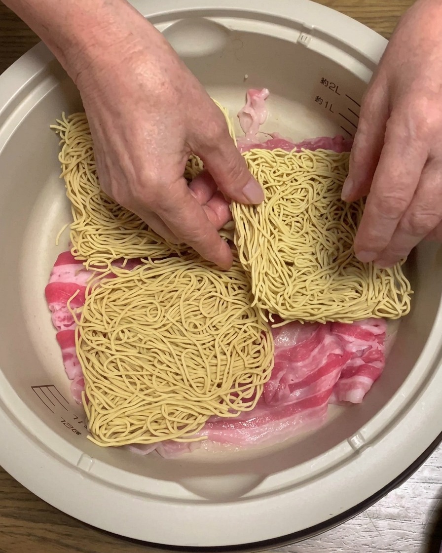 Kostki suchego makaronu ramen układane na warstwie boczku w garnku.