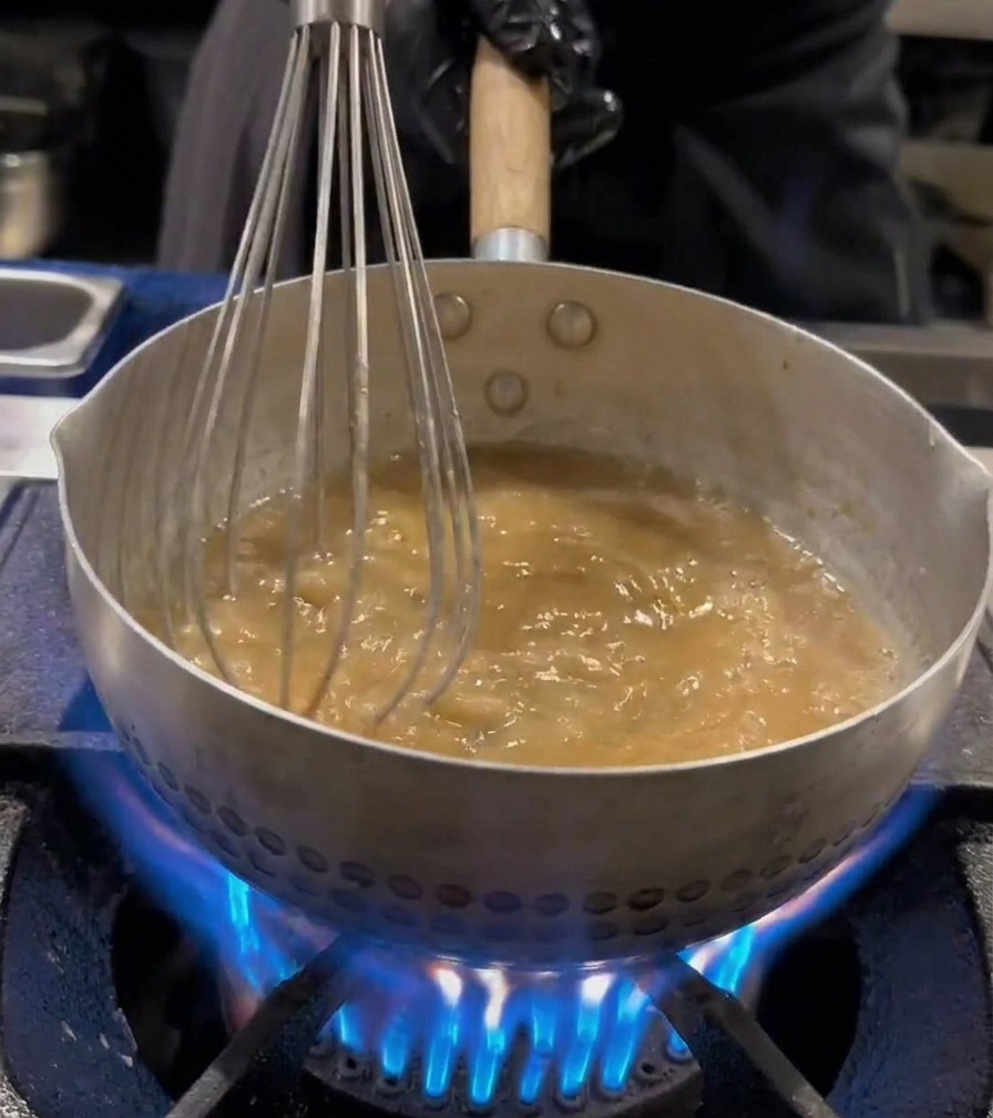 Makaron ramen mieszany trzepaczką w garnku z wrzącą wodą.