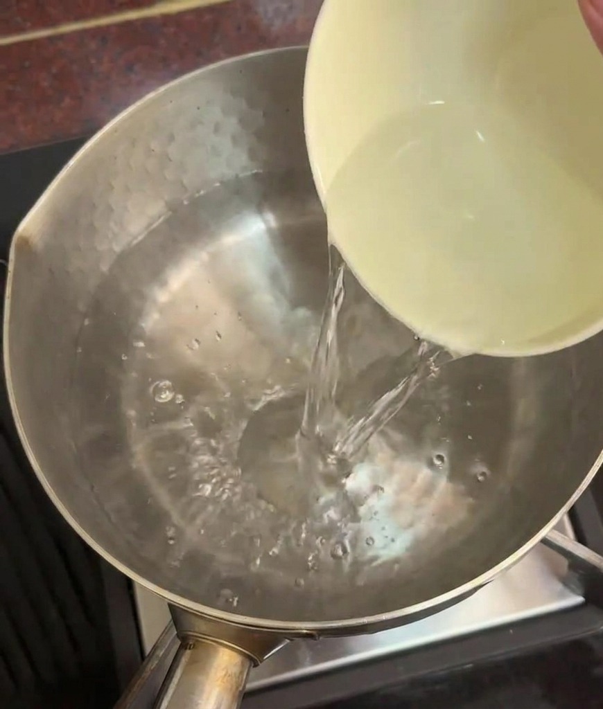 Osoba wlewająca ceramiczną miskę czystej wody do garnka z gorącą wodą na płycie kuchennej.