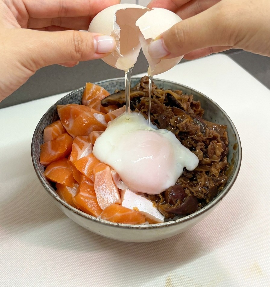 Dłonie ostrożnie rozbijające skorupkę jajka, by wbić miękkie jajko onsen na środek miski z donburi.
