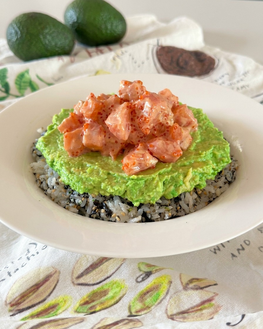 Poke bowl z widocznymi warstwami ryżu, zielonej pasty z awokado i różowych, lśniących kostek łososia.