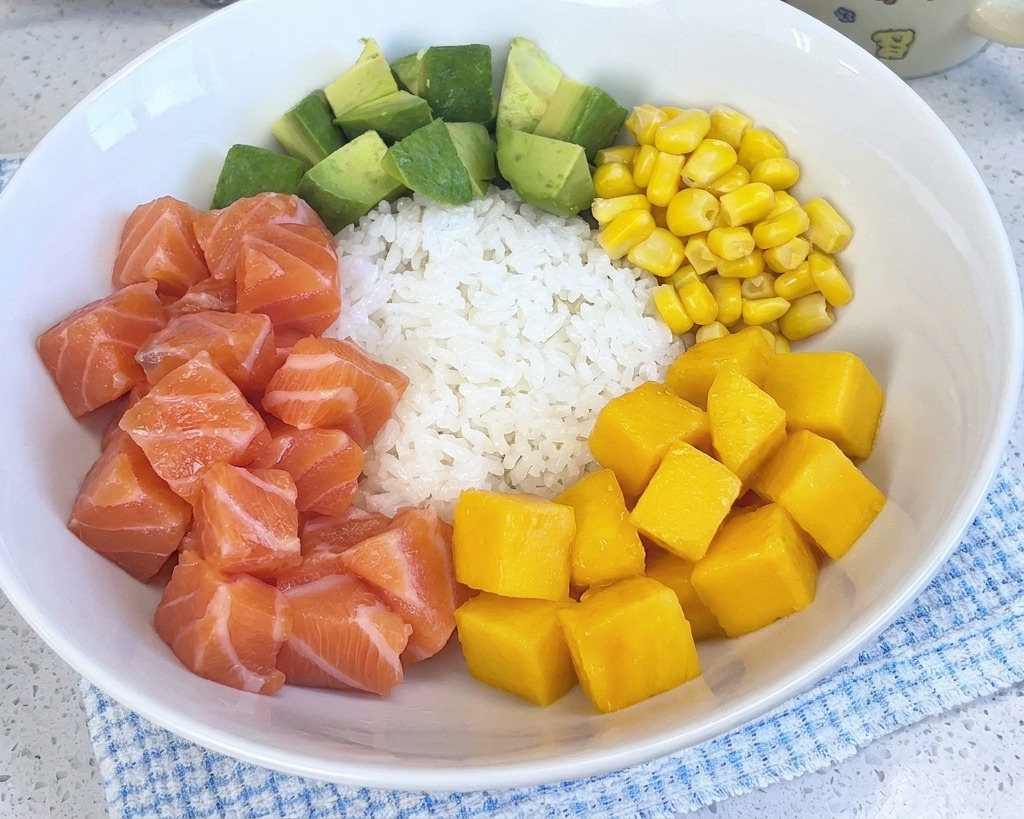 Kolorowe poke bowl z białym ryżem, łososiem, awokado, kukurydzą i krewetkami, wzbogacone teraz o porcję jaskrawożółtych kostek mango.