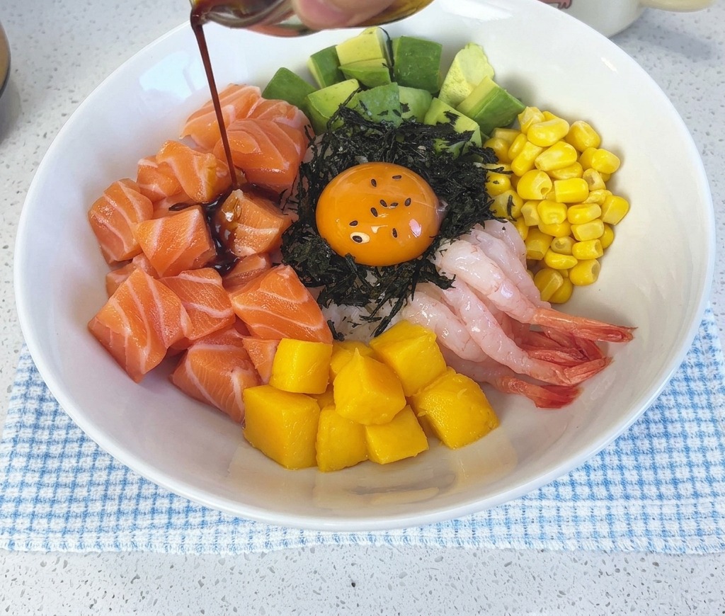 Ciemny sos sojowy z wasabi wylewany z małej szklanej miseczki na skomponowane poke bowl z łososiem i żółtkiem.