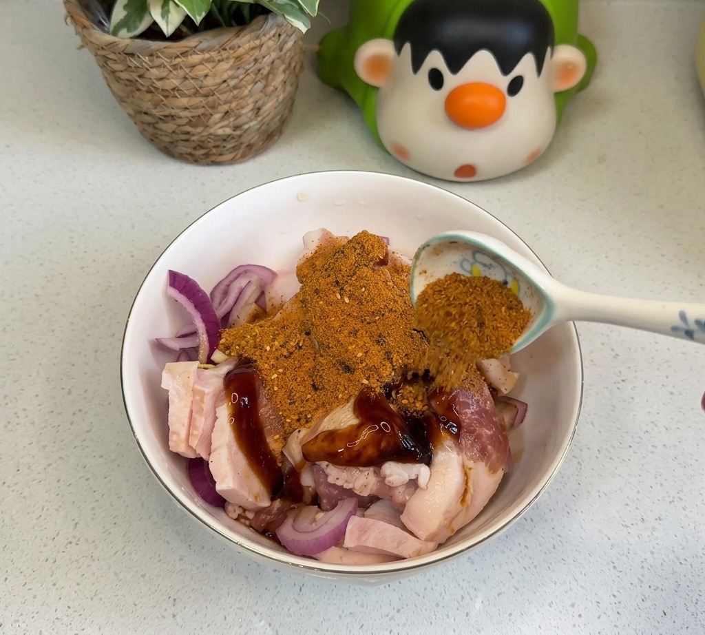 Łyżka pomarańczowej przyprawy BBQ i czerwonego chili w proszku posypywana na zamarynowany boczek z cebulą.