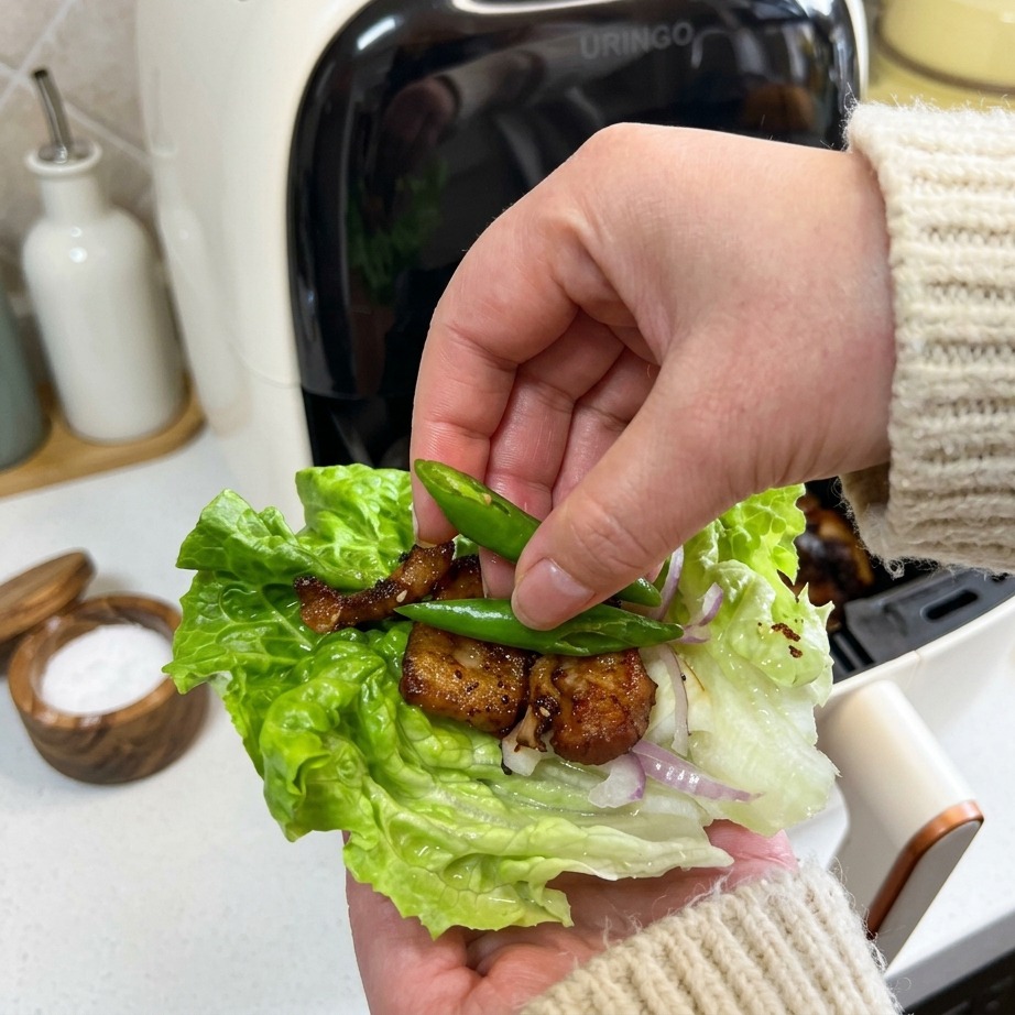 Dłoń kładąca dwie małe, jasnozielone papryczki chili na wrap z sałaty z chrupiącym boczkiem i cebulą.