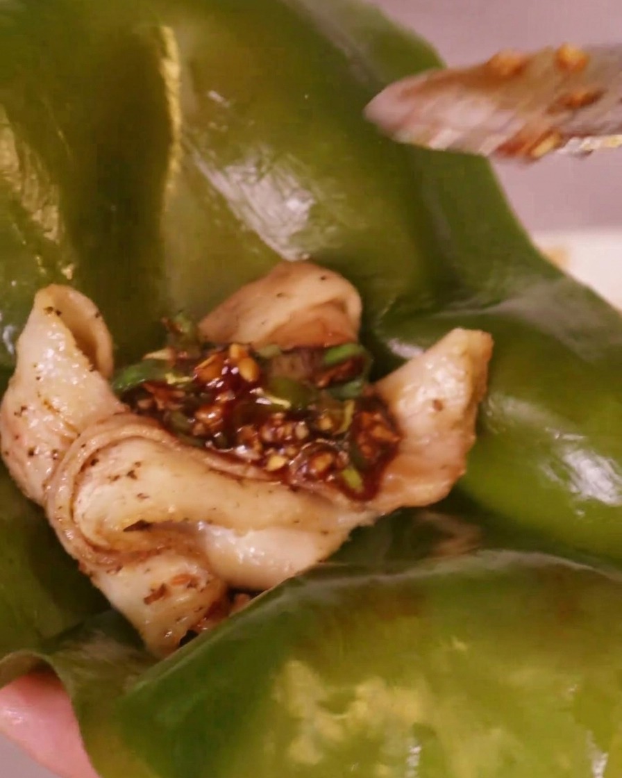 Porcja ostrego czerwonego sosu chili nakładana na kawałek grillowanego boczku spoczywający na zielonym liściu wodorostu kelp.