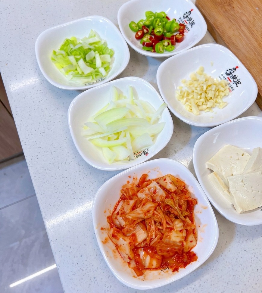 Małe białe miseczki z posiekaną dymką, papryczkami, czosnkiem, cebulą, tofu i kimchi.