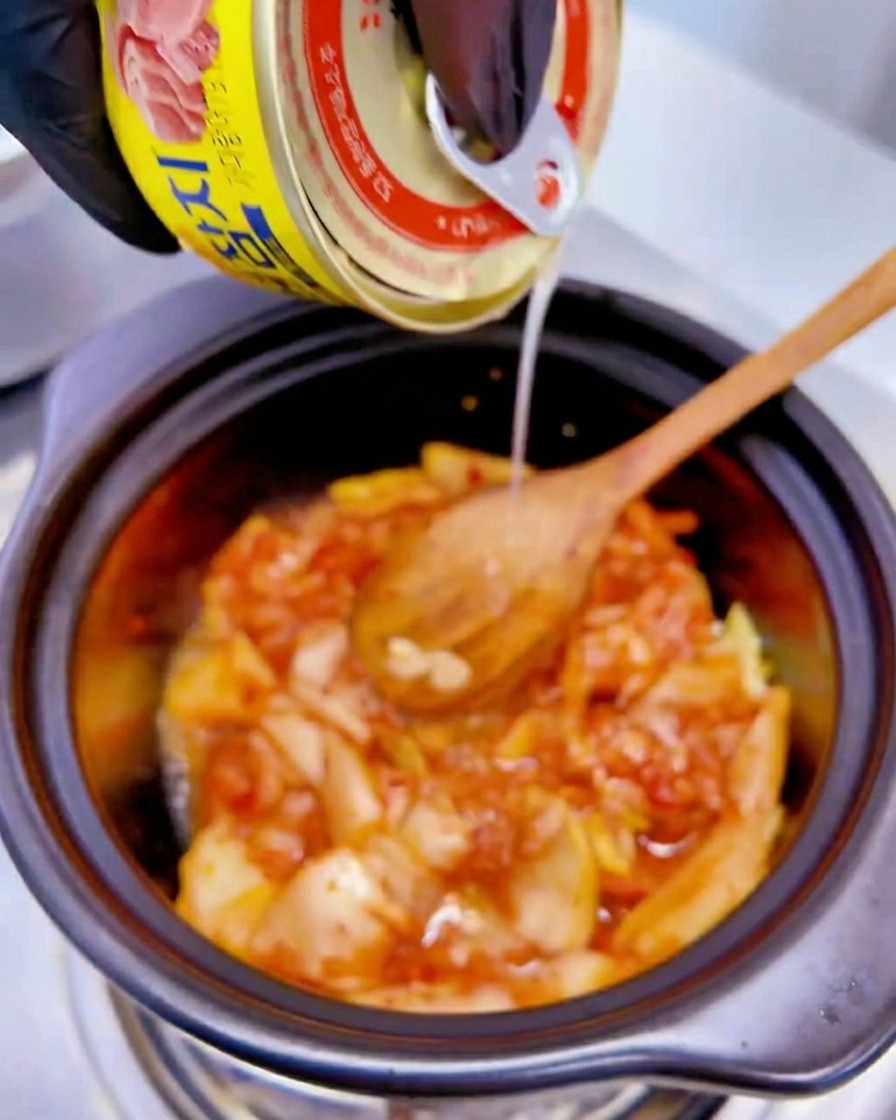 Płyn z żółtej puszki tuńczyka wlewany do garnka z podsmażanym kimchi.