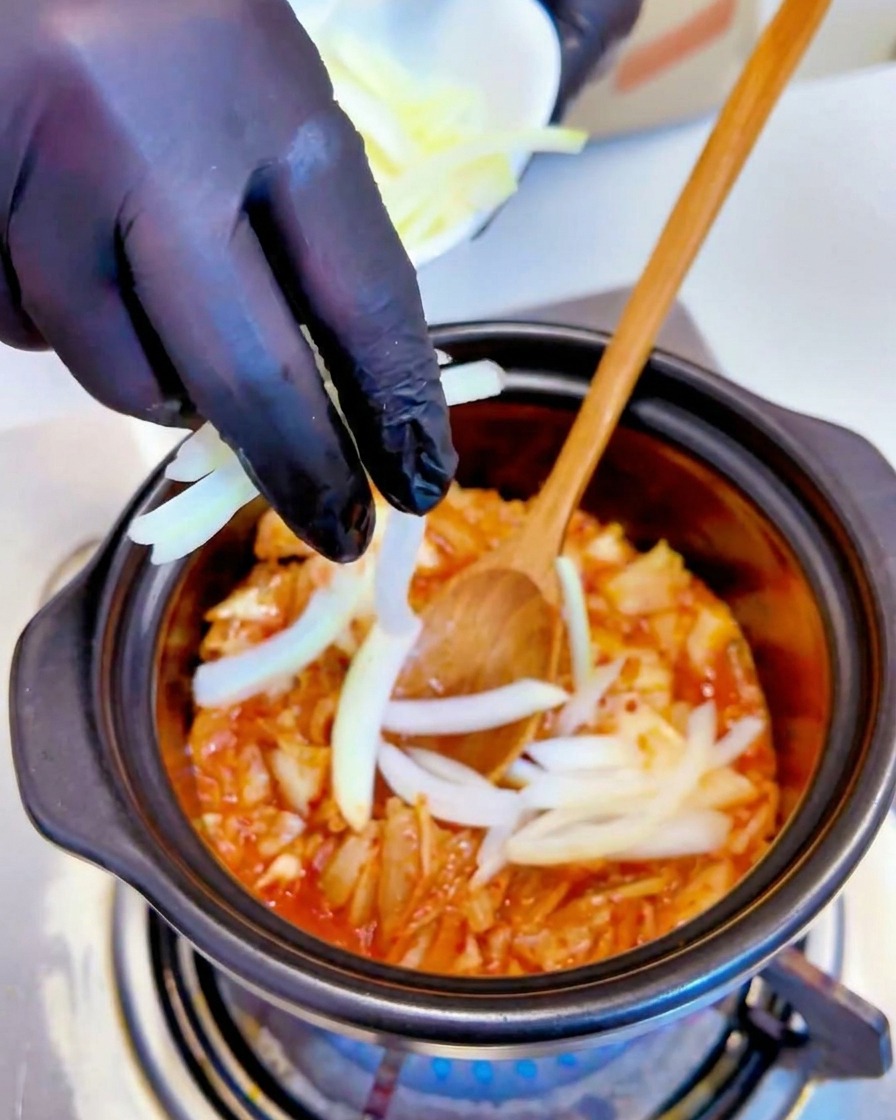 Pokrojona w piórka biała cebula dodawana do duszącego się kimchi w garnku.