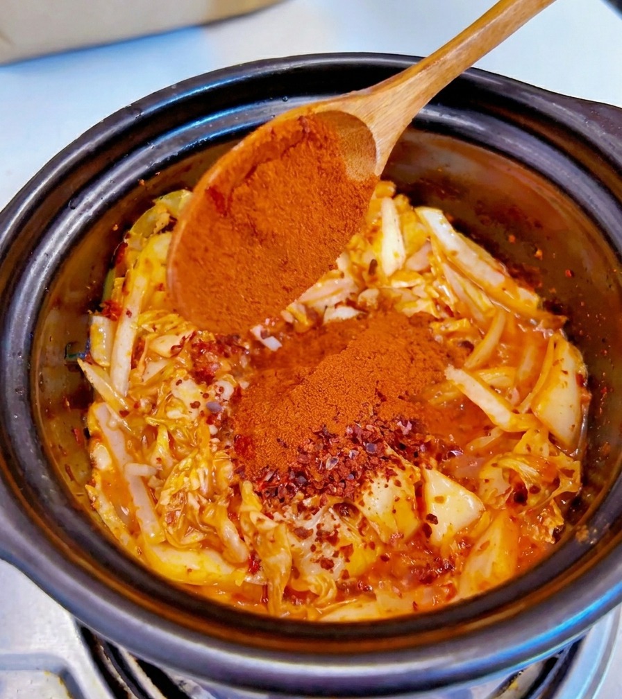 Drobno mielone czerwone chili sypane z drewnianej łyżki na doprawioną mieszankę kimchi i cebuli.