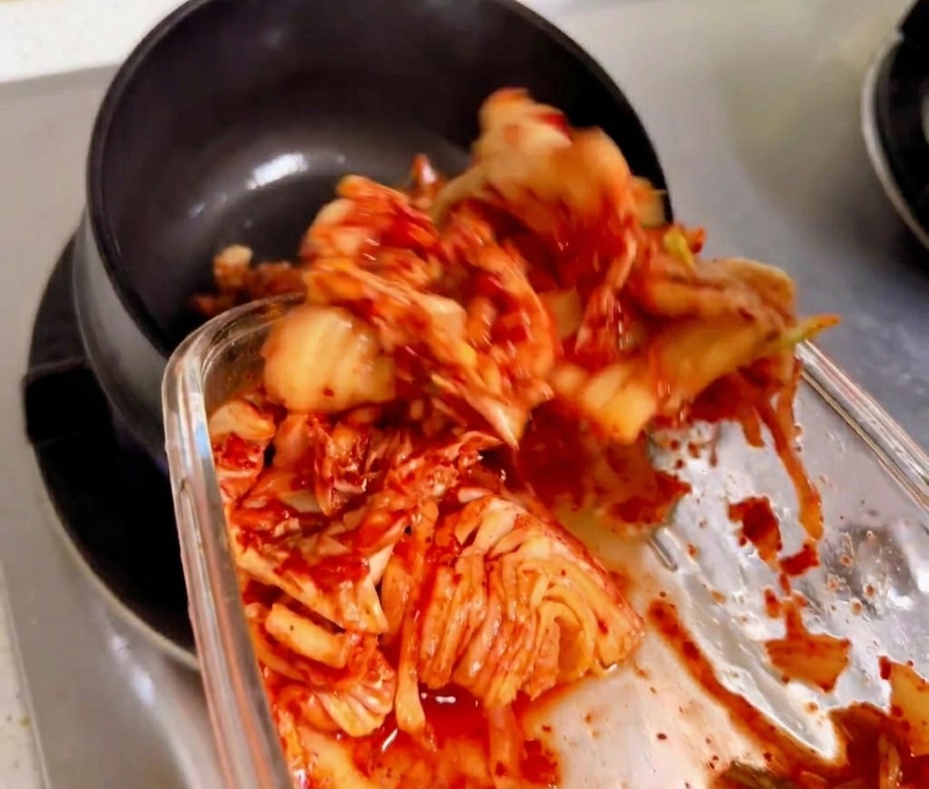 Pokrojone kimchi mieszane i smażone w tradycyjnym czarnym kamiennym garnku na gazie.