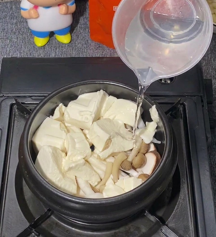 Czysta woda nalewana z plastikowej miarki do czarnego garnka z tofu i grzybami.