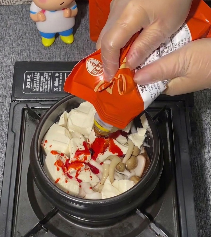 Ręka w przezroczystej rękawiczce wyciska z saszetki jaskrawoczerwoną pastę na miękkie tofu.