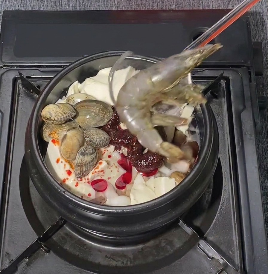 Dwie duże, surowe krewetki delikatnie układane w bulgoczącym koreańskim gulaszu z tofu i owocami morza.