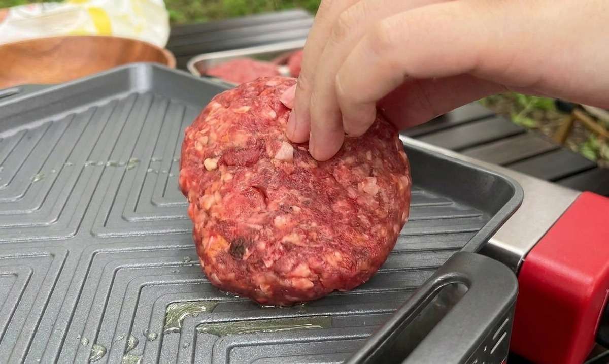 Nakładanie grubego, surowego kotleta na gorącą, żeliwną patelnię grillową podczas gotowania na zewnątrz.