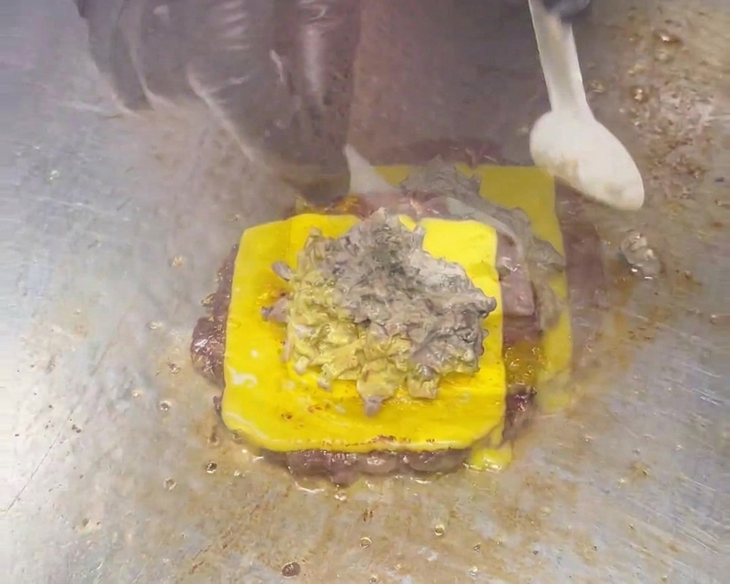 Łyżka rozprowadza gęsty, kremowy, szarobrązowy sos grzybowy na cheeseburgerze.