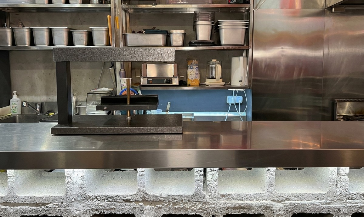 Czarny elektryczny podgrzewacz do sera raclette stojący w gotowości na gastronomicznym blacie ze stali nierdzewnej.