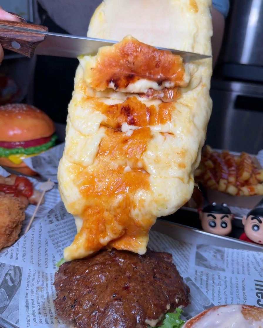 Obfita warstwa stopionego, przypieczonego sera zeskrobywana nożem z dużego kręgu bezpośrednio na kotlet wołowy w burgerze.