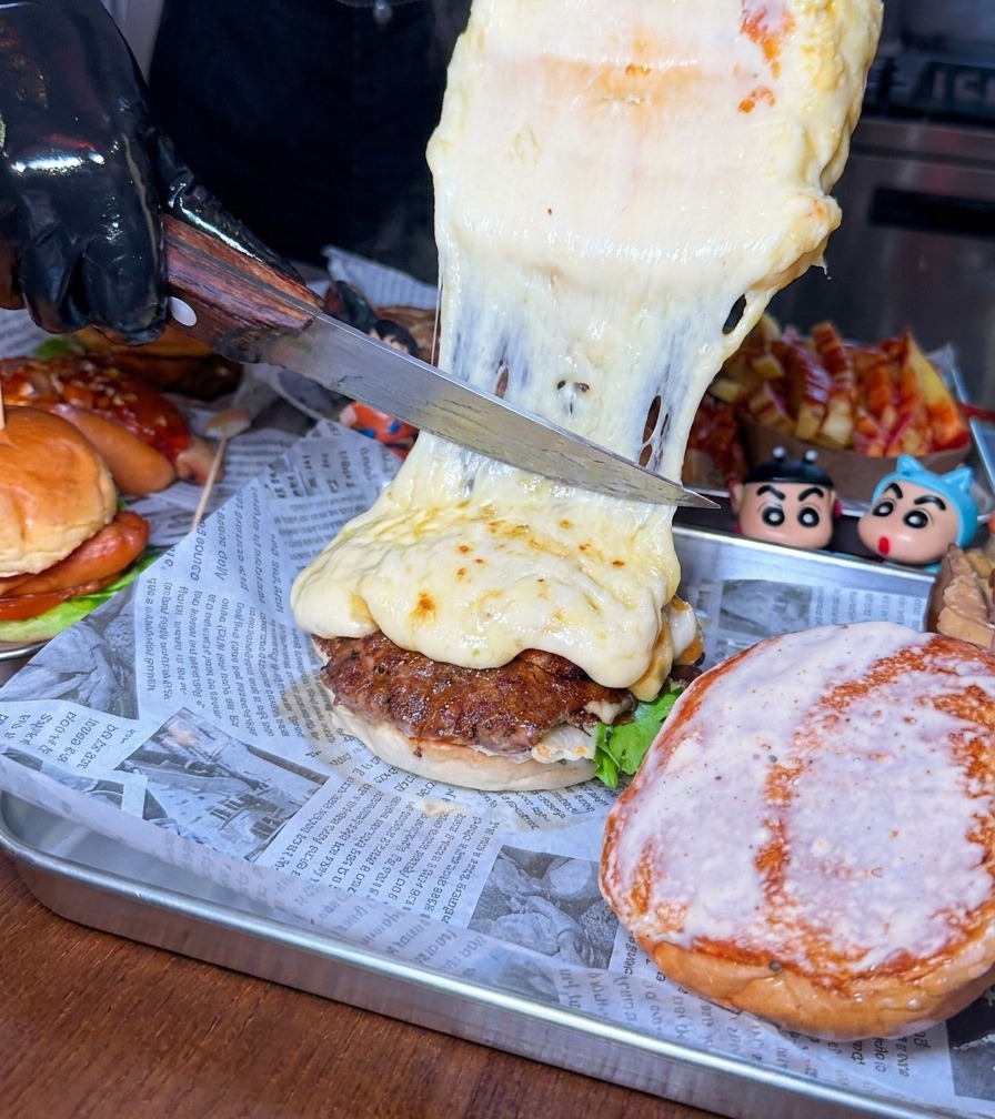 Duży nóż zeskrobujący grubą warstwę stopionego, bąbelkującego sera z kręgu na kotlet wołowy w burgerze.