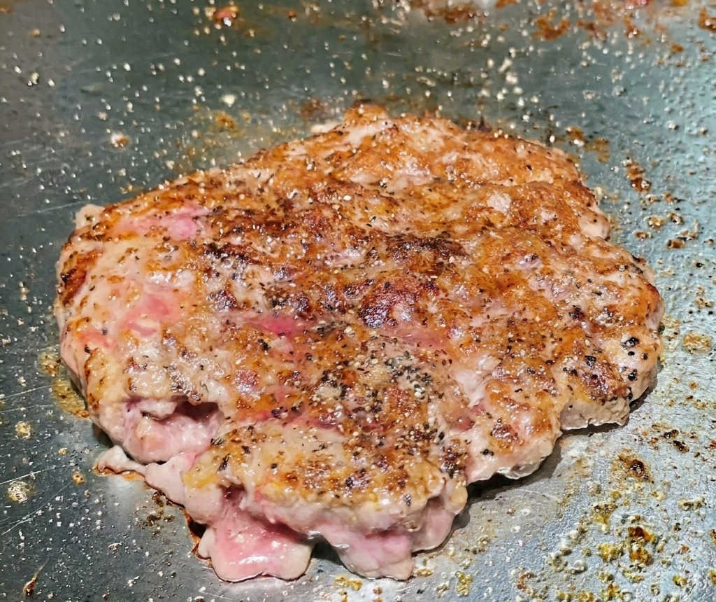 Obrócony kotlet wołowy na grillu wykazujący mocno wysmażoną, brązową i chrupiącą powierzchnię.