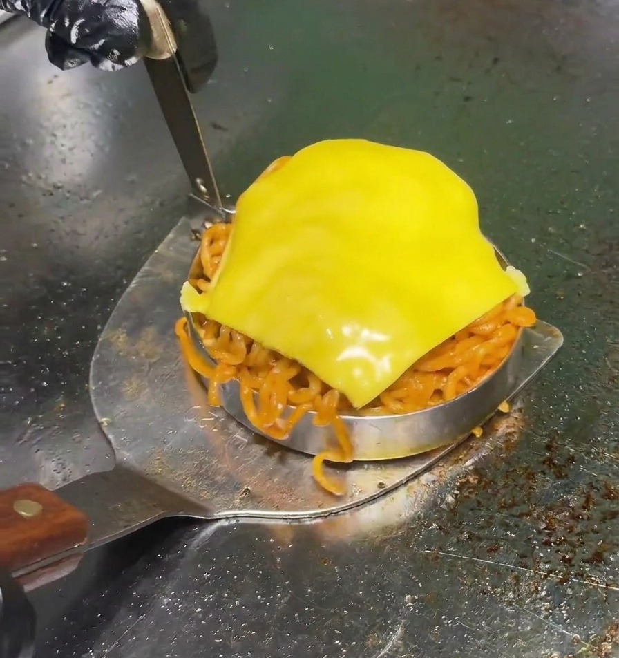 Metalowa łopatka podnosząca okrągły ring wypełniony pikantnym czerwonym makaronem z plasterkiem żółtego sera na profesjonalnym grillu.