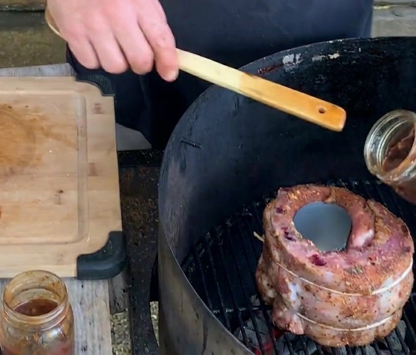 Dłoń wlewająca gęsty, ciemny sos jagodowy ze szklanego słoika do metalowej puszki umieszczonej wewnątrz koszyczka z żeberka na grillu.