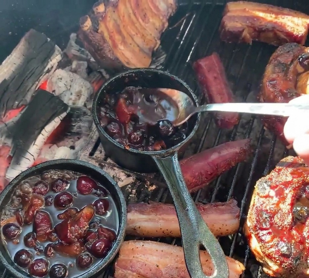 Osoba nakładająca łyżką ciemny sos jagodowy z małego żeliwnego garnuszka na grillowane koszyczki z żeberek wypełnione ziemniakami.