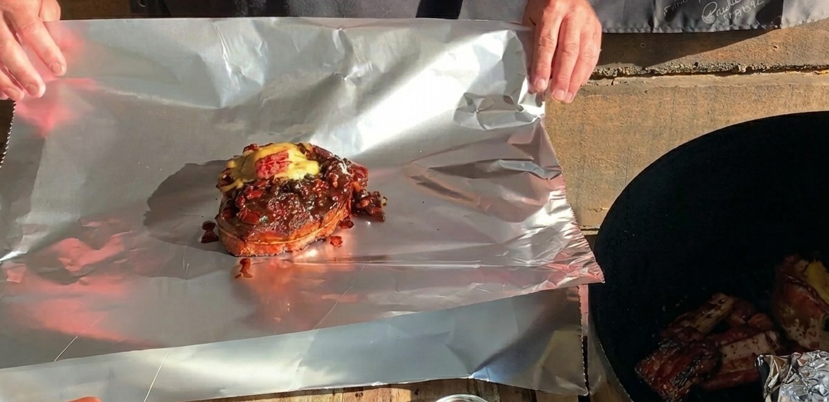 Gotowy koszyczek BBQ z żeberka zwieńczony roztopionym serem leży na dużym arkuszu folii aluminiowej, gotowy do zawinięcia.