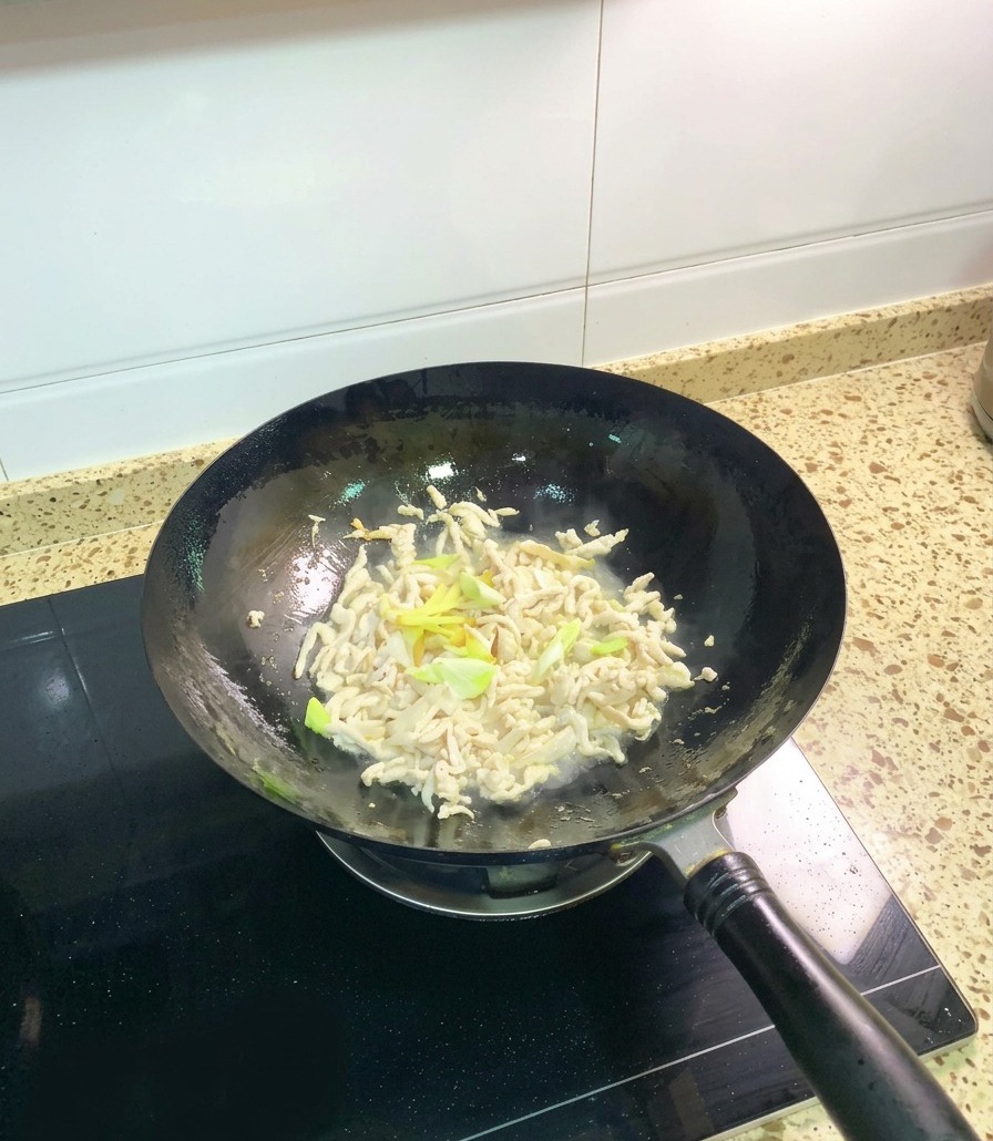 Matowe, częściowo usmażone kawałki kurczaka mieszane w woku ze świeżą zieloną cebulką i plastrami imbiru.