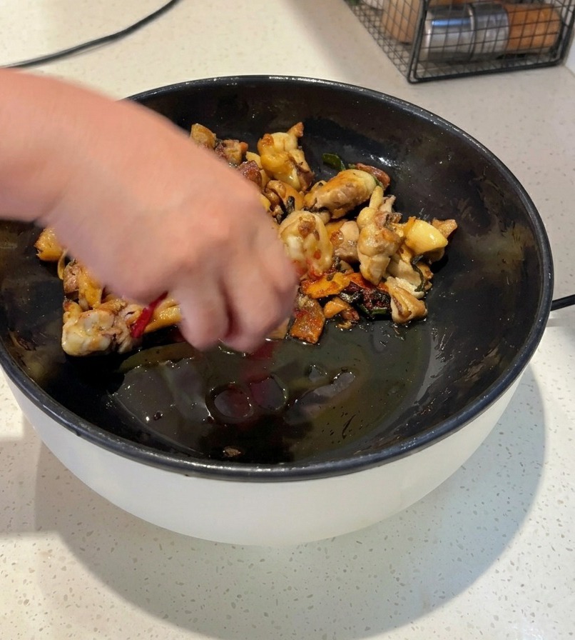 Osoba smażąca kawałki kurczaka na czarnej patelni z całymi suszonymi czerwonymi papryczkami chili i jaskrawoczerwonym chili w proszku.