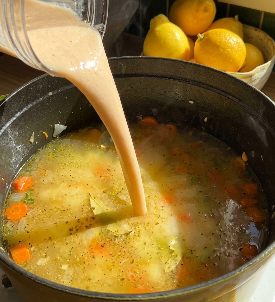 Strumień gęstego, kremowego purée z fasoli wlewany z blendera do garnka z mrugającą zupą i marchewką.