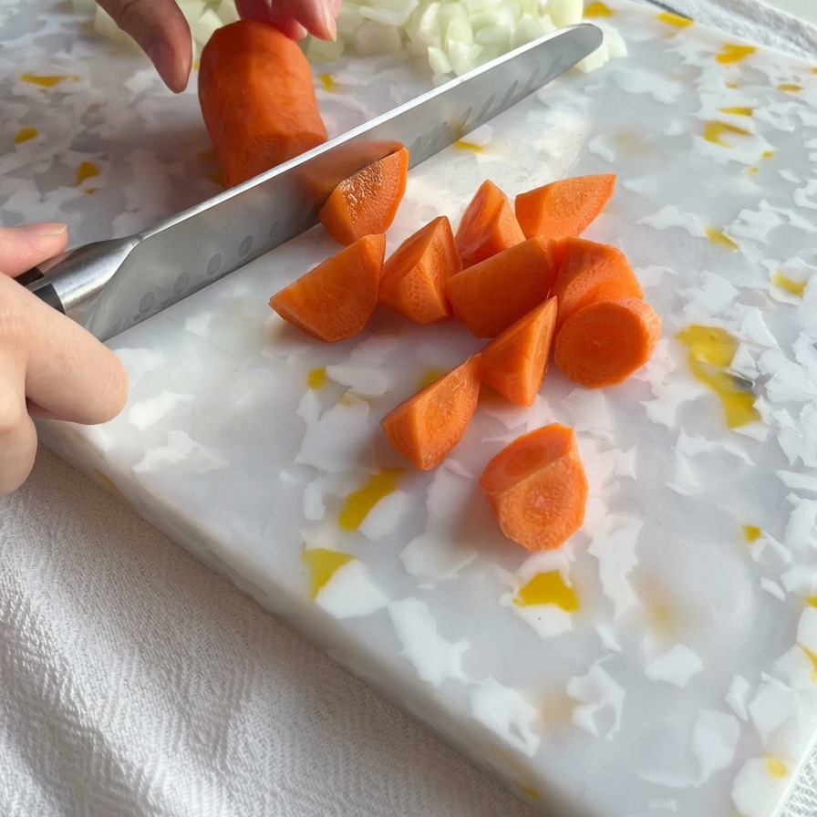 Nóż kuchenny krojący jasnopomarańczową marchewkę na kawałki na desce obok posiekanej białej cebuli.