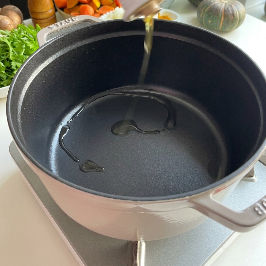 Olej do smażenia nalewany z białej ceramicznej butelki do rozgrzanego, czarnego żeliwnego garnka Staub.