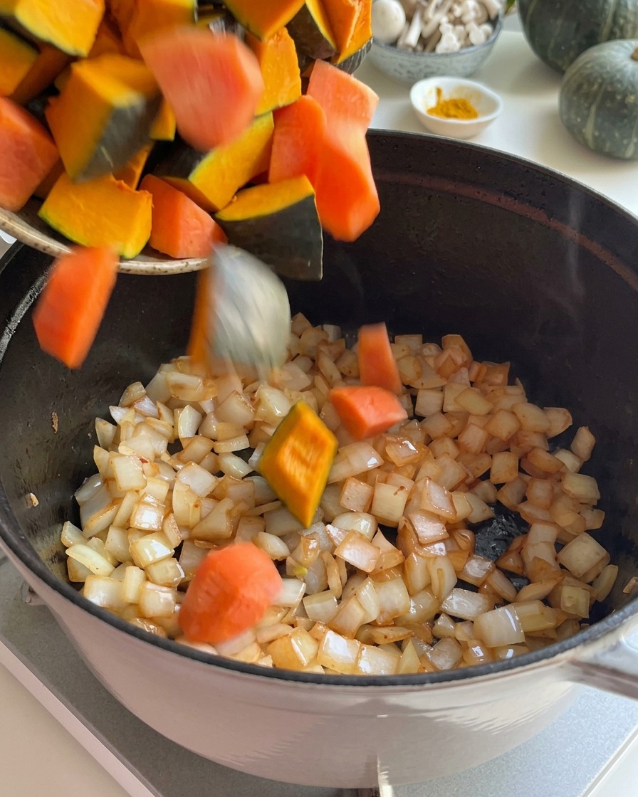 Kawałki świeżej dyni i pokrojona marchewka dodawane do podsmażonej cebuli w garnku.