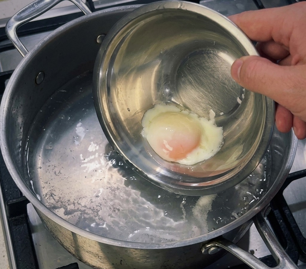 Mała miseczka z ugotowanym jajkiem sous vide wkładana do garnka z gorącą wodą w celu ścięcia zewnętrznego białka.