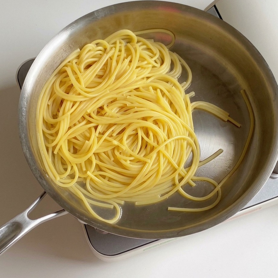 Widok z góry na ugotowany, odcedzony makaron spaghetti na patelni, z małą kostką żółtego masła roztapiającą się na środku.