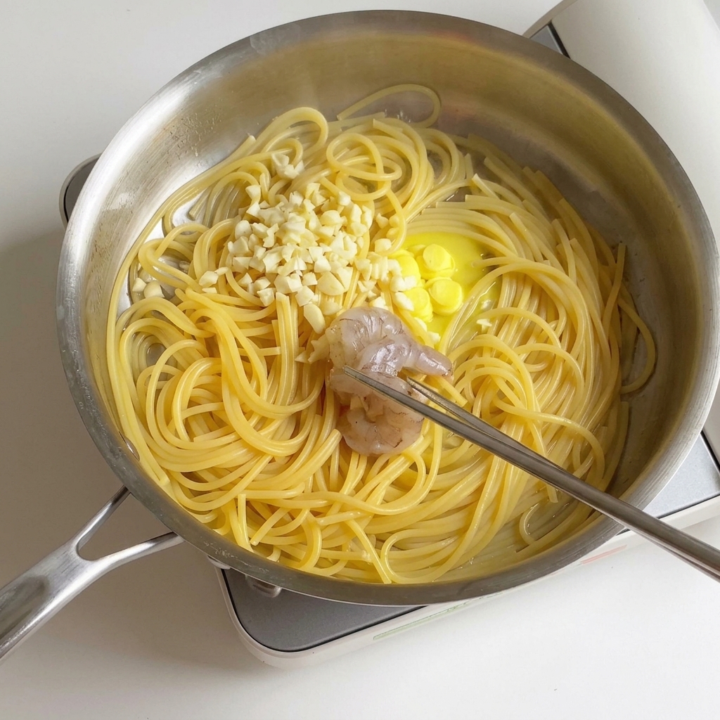 Zamarynowane krewetki przekładane na patelnię z ugotowanym spaghetti, rozpuszczonym masłem i posiekanym czosnkiem.
