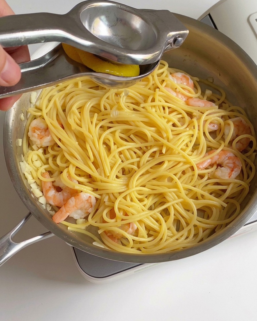 Świeży sok z cytryny wyciskany z metalowego wyciskacza do cytrusów na patelnię z usmażonymi krewetkami i spaghetti.